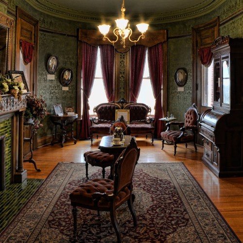 Victorian-style parlor with ornate furniture, a chandelier, and decorative wallpaper, featuring a cozy, elegant atmosphere.