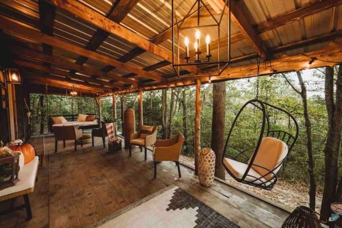 Cozy outdoor seating area with a swing chair, wooden beams, and lush greenery in the background.