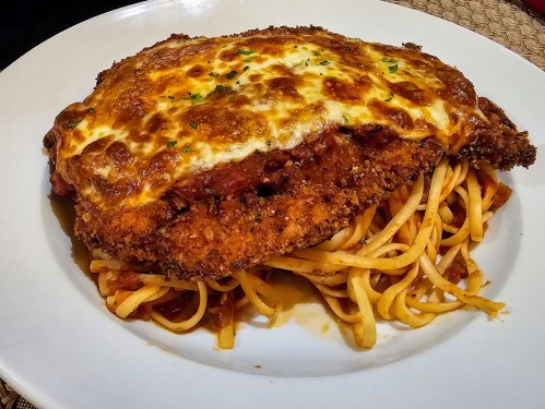 A plate of spaghetti topped with a crispy chicken cutlet and melted cheese, garnished with herbs.