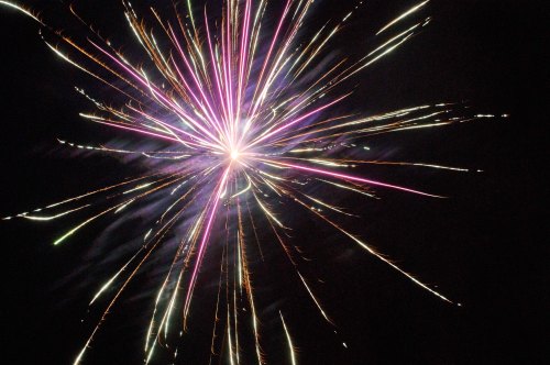 A vibrant firework explosion with purple and white sparks radiating against a dark night sky.