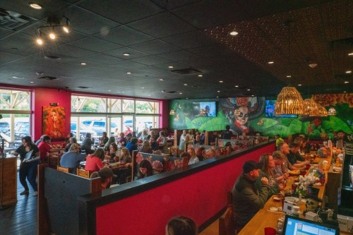 A busy restaurant interior with colorful murals, filled with diners at tables and booths, creating a lively atmosphere.
