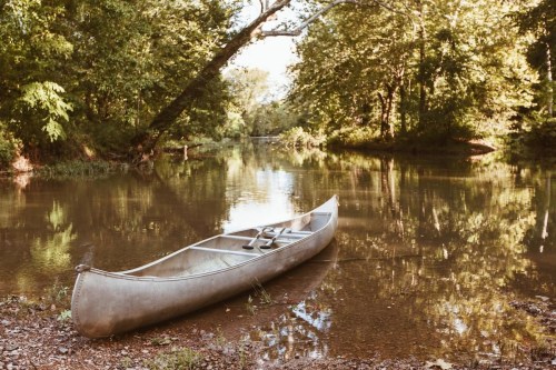 A canoe rests on the calm waters of a tree-lined river, surrounded by lush greenery.