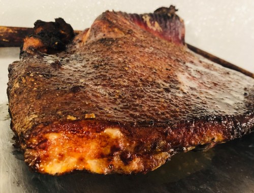 Close-up of a perfectly cooked, seasoned brisket with a crispy, caramelized crust on a metal tray.