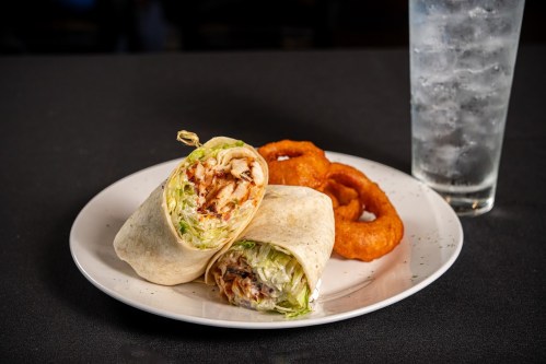A plate with two chicken wraps, lettuce, and onion rings, alongside a glass of water.