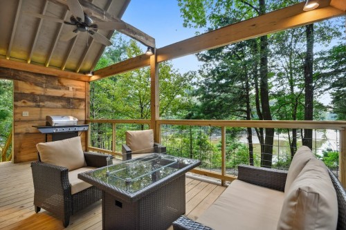 Cozy outdoor seating area with a glass table, overlooking trees and a grill on a wooden deck.