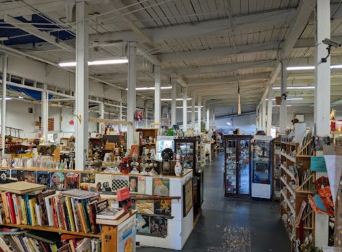 A spacious antique store filled with shelves of books, collectibles, and various vintage items under bright lighting.
