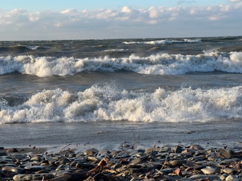 Waves crash onto a rocky shore under a cloudy sky, creating a dynamic seascape.