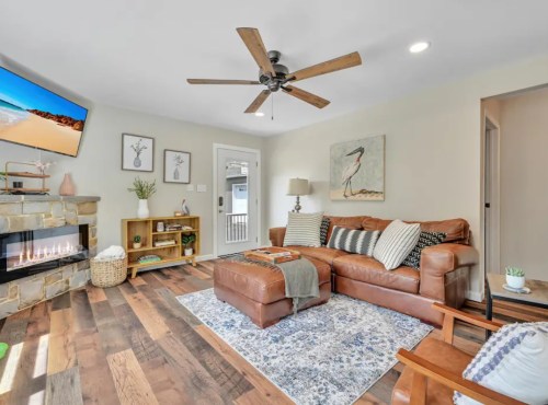Cozy living room with a leather sofa, wooden floor, TV, and decorative elements, featuring a stone fireplace and artwork.