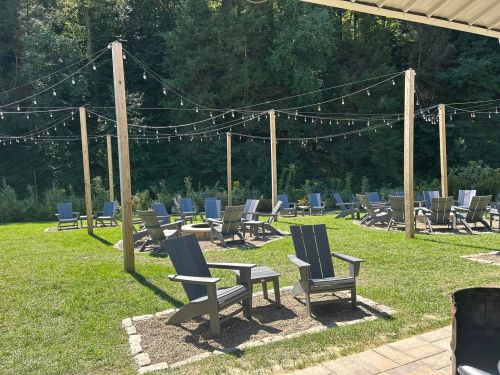 Outdoor seating area with wooden chairs and string lights, surrounded by greenery and trees.