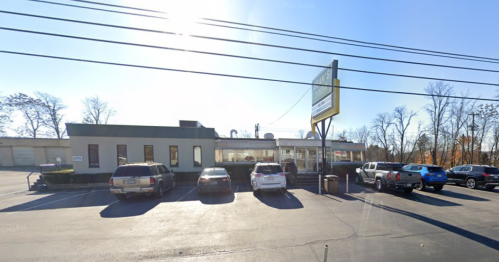 A restaurant building with large windows, surrounded by parked cars and trees, under a clear blue sky.