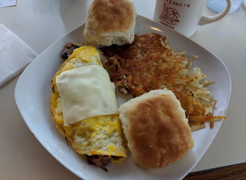 A plate with an omelette topped with cheese, two biscuits, and hash browns on the side.