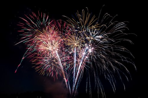 Colorful fireworks burst in the night sky, creating a vibrant display of light and color against a dark background.