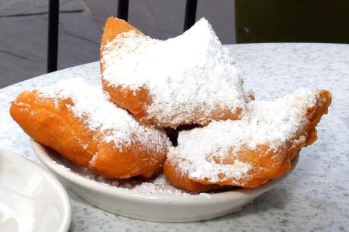 A plate of three golden-brown beignets dusted with powdered sugar.