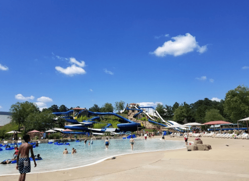 A sunny water park scene with slides, a sandy beach area, and people enjoying the water.