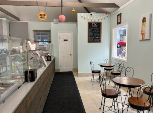 Interior of an ice cream shop featuring a service counter, tables, and a menu board on the wall.