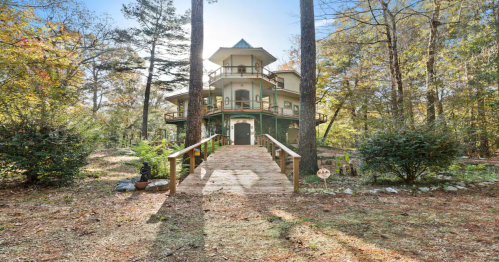 A charming multi-story house surrounded by trees, with a wooden walkway leading to the entrance.