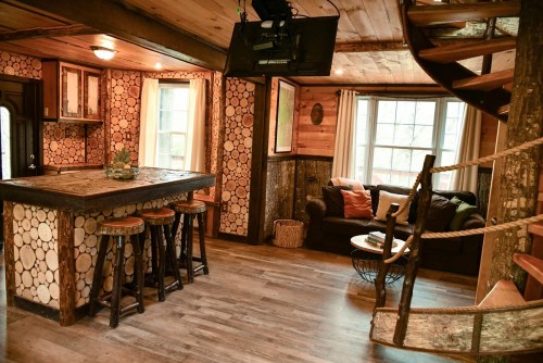 Cozy interior of a rustic cabin featuring a wooden bar, spiral staircase, and comfortable seating area.