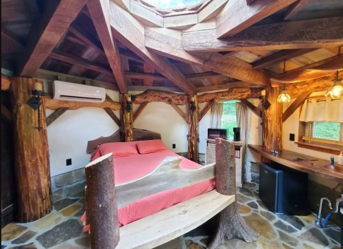 Cozy wooden cabin interior featuring a bed, stone floor, and rustic decor with natural light from a skylight.