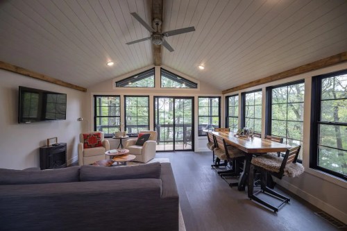 Bright, modern living space with large windows, a dining table, and cozy seating, surrounded by greenery.