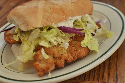 A crispy chicken sandwich with lettuce, onions, and mayonnaise on a soft roll, served on a plate.