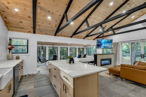 Modern living room with a vaulted ceiling, large windows, a cozy sofa, and a TV above a stylish fireplace.