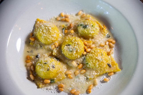 A plate of yellow ravioli topped with pine nuts and grated cheese in a creamy sauce.
