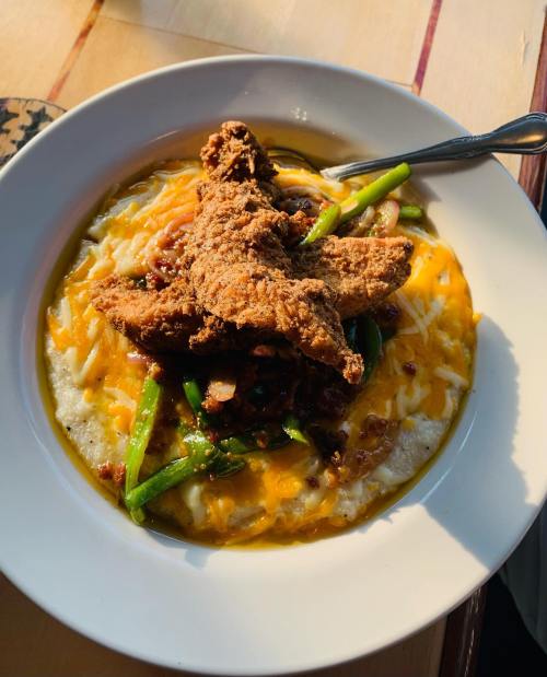 A bowl of creamy grits topped with fried chicken, green beans, and melted cheese.