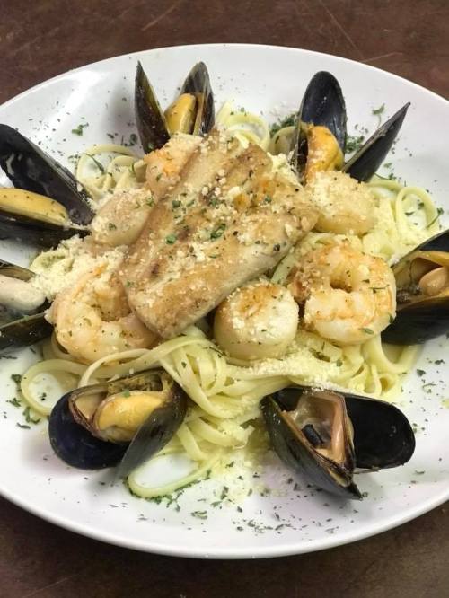 A plate of pasta topped with shrimp, fish, and mussels, garnished with herbs and grated cheese.