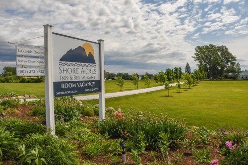 Sign for Shore Acres Inn & Restaurant with a scenic view of green lawns and trees under a cloudy sky. Room vacancy available.