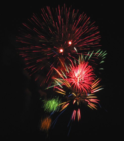 Colorful fireworks explode in the night sky, creating vibrant bursts of red, green, and yellow against a dark background.