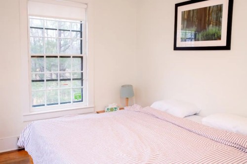 A cozy bedroom with a striped bedspread, a lamp, and a large window letting in natural light.