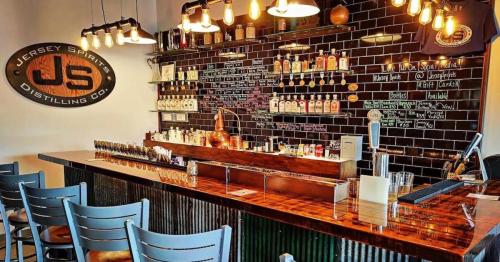 A stylish bar with a wooden counter, shelves of spirits, and warm lighting in a distillery setting.