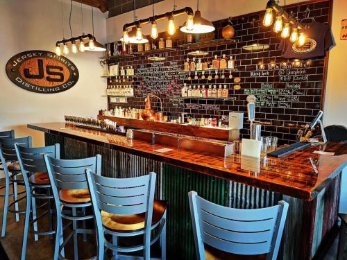 A rustic bar with a wooden counter, shelves of spirits, and industrial decor, featuring stools and warm lighting.