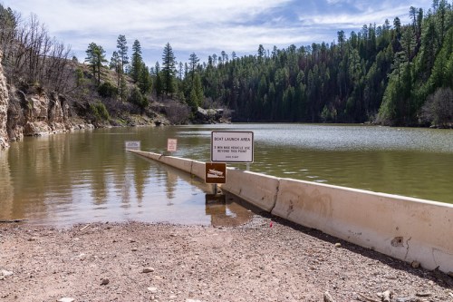 A calm lake surrounded by trees, with a boat launch area sign and a concrete ramp leading into the water.