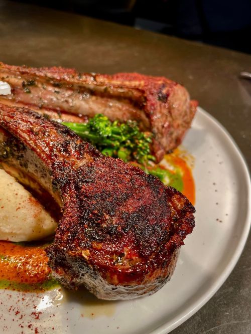 A close-up of a beautifully plated meat dish featuring a seasoned chop, mashed potatoes, and vibrant green vegetables.