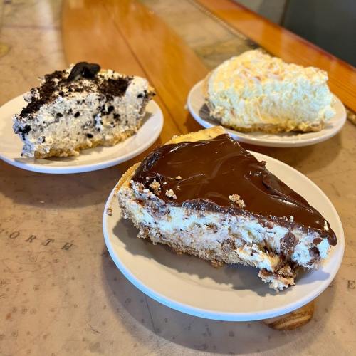 Three slices of dessert on white plates: one chocolate, one cream, and one cookies and cream.
