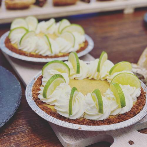 Two lime pies with whipped cream and lime slices, displayed on a wooden surface.