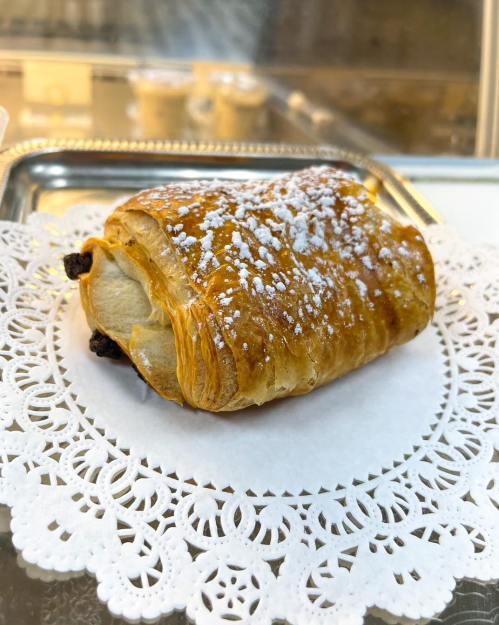 A golden-brown pastry dusted with powdered sugar, resting on a decorative lace paper.