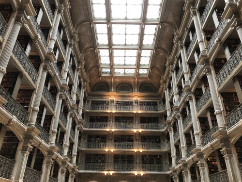 A grand library interior with tall shelves, ornate architecture, and a glass ceiling allowing natural light.