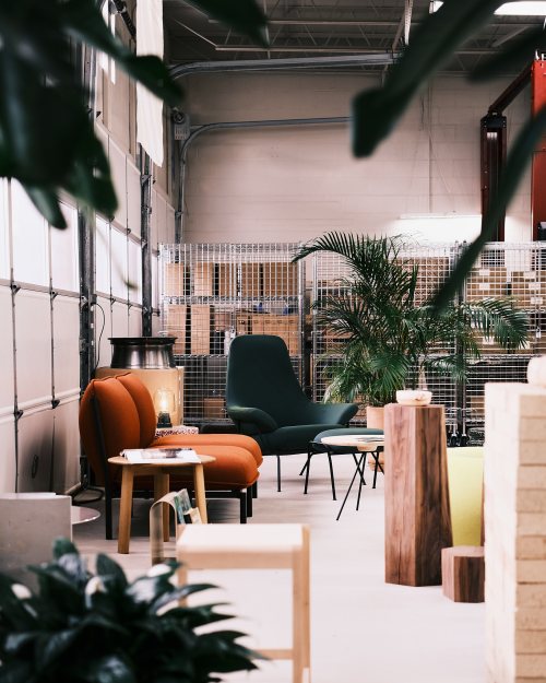 A cozy interior with modern furniture, including orange chairs, a green armchair, and plants in a spacious setting.