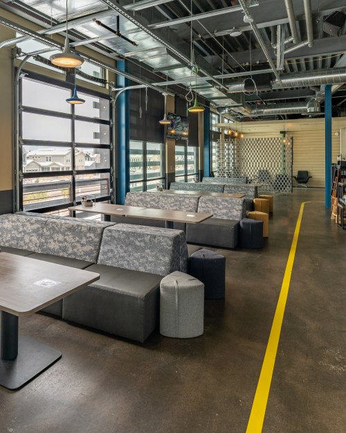 Modern restaurant interior with booth seating, tables, and large windows, featuring a clean, industrial design.