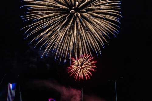 Colorful fireworks burst in the night sky, with blue and red explosions above a dark background.