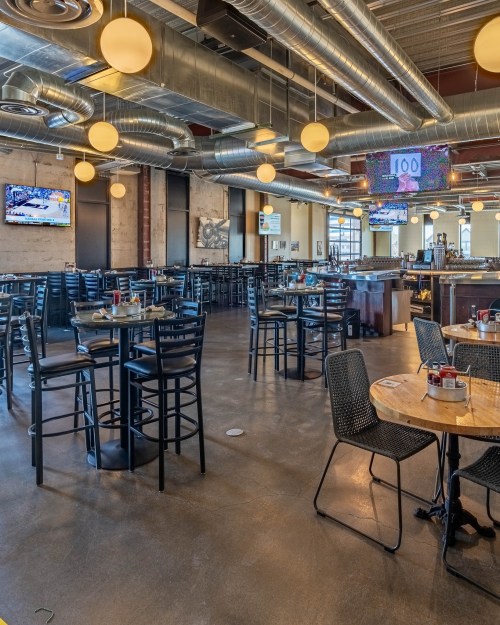 A spacious restaurant interior with tables, chairs, and large screens displaying sports events.
