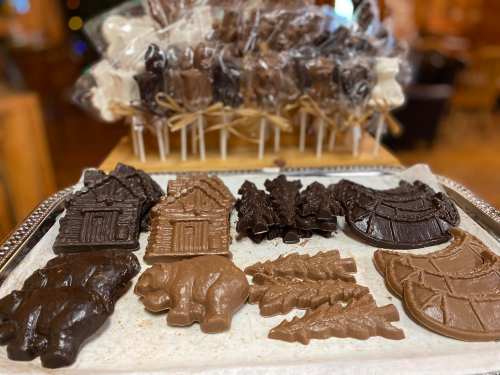 A tray of assorted chocolate shapes, including houses, trees, and bears, with chocolate lollipops in the background.