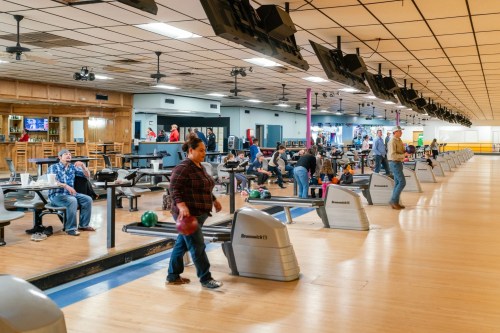 A busy bowling alley with people bowling, sitting at tables, and enjoying the atmosphere.