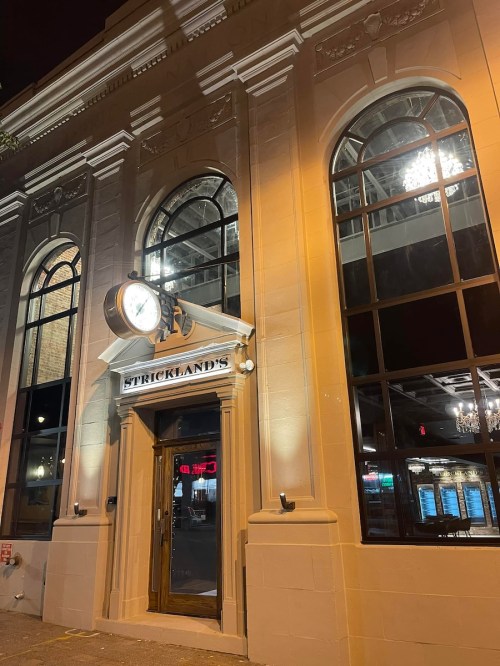 Exterior of Strickland's restaurant at night, featuring large arched windows and a prominent clock above the entrance.