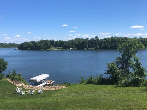 A serene lake view with a dock, boats, and green trees under a clear blue sky.