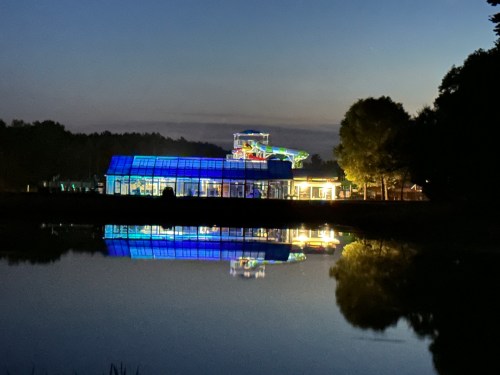 A brightly lit building at night, reflecting in a calm lake, surrounded by trees.