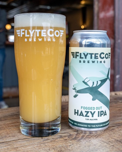 A glass of hazy IPA next to a can labeled "Fogged Out Hazy IPA" from FlyteCo Brewing.