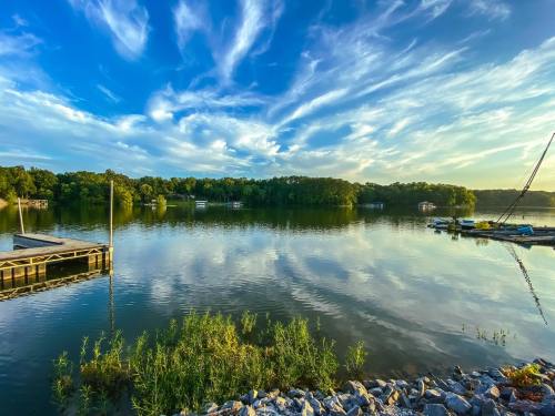 A serene lake scene with a wooden dock, lush greenery, and a vibrant sky reflecting on the water's surface.